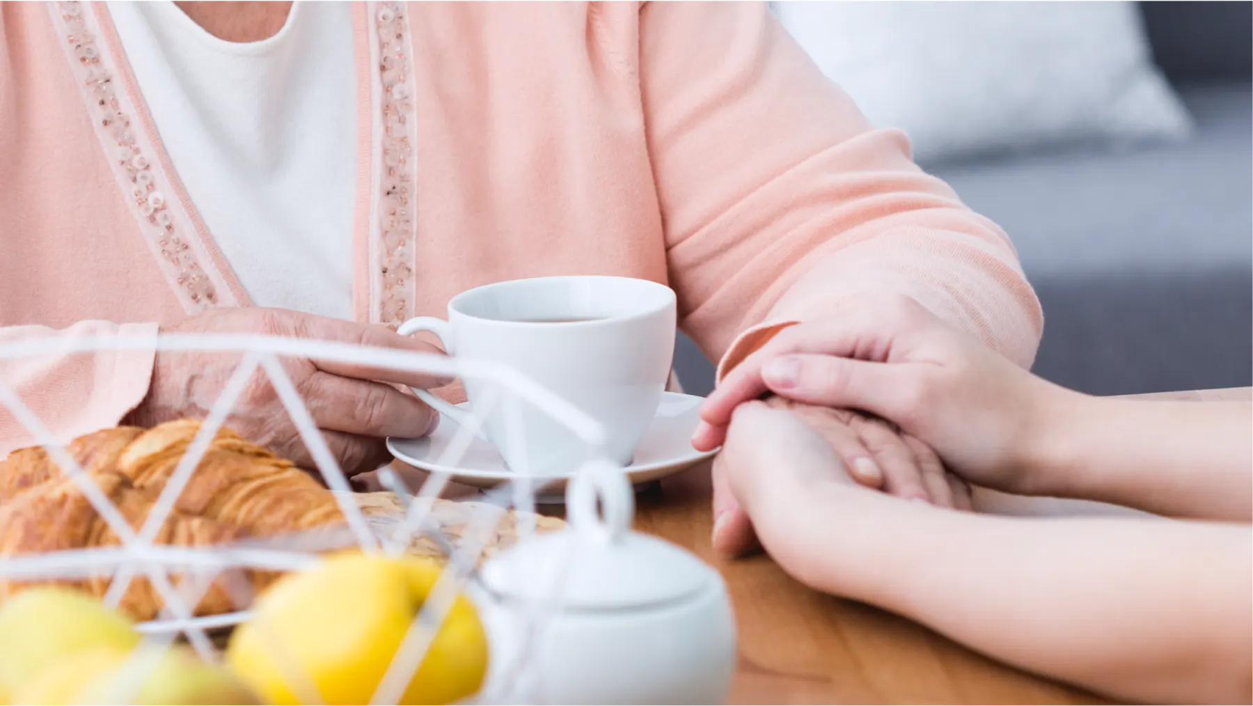 A caregiver holding an older woman's hand at the breakfast table